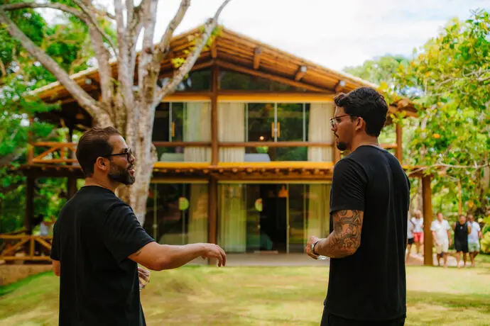 Anfitriões conversando diante da casa de madeira